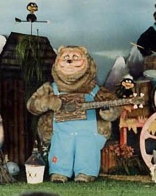 Billy Wilbur (older Billy Bob) animatronic. He is a fat grey bear with denim overalls and a cheap wooden bass.