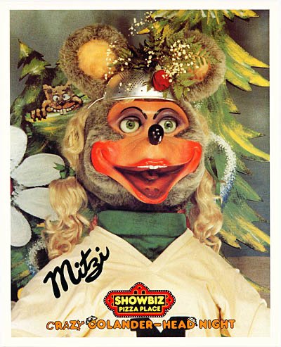 A photo of Mitzi Mozzarella animatronic wearing a decorated colander on her head. She is surrounded by a frame saying 'Crazy Colander Head Night' and the image has her signature.